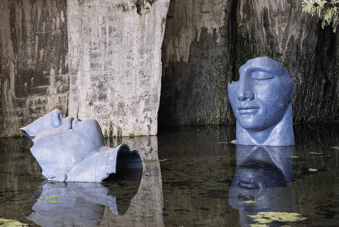 Zwei übergroße Kopfskulpturen in einer Höhle in flachem Wasser